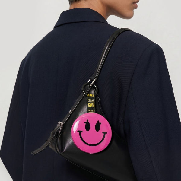 Person wearing a black leather bag with a pink smiley face patch on a plain background S.W.Smiley X Fancii & Co.  Lighted Charm Mirror with 1x and 10x magnification bag clip in Pink 